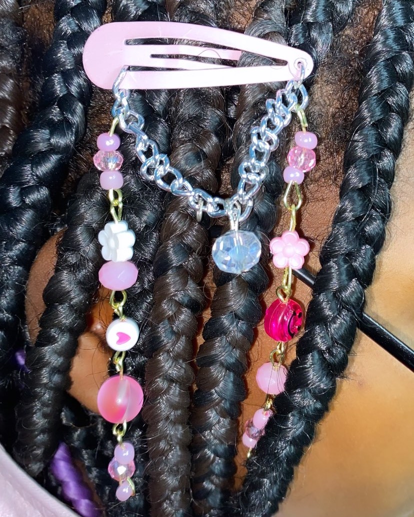 Close-up of dark braided hair with a pink hair clip and two decorative chains with beads and charms